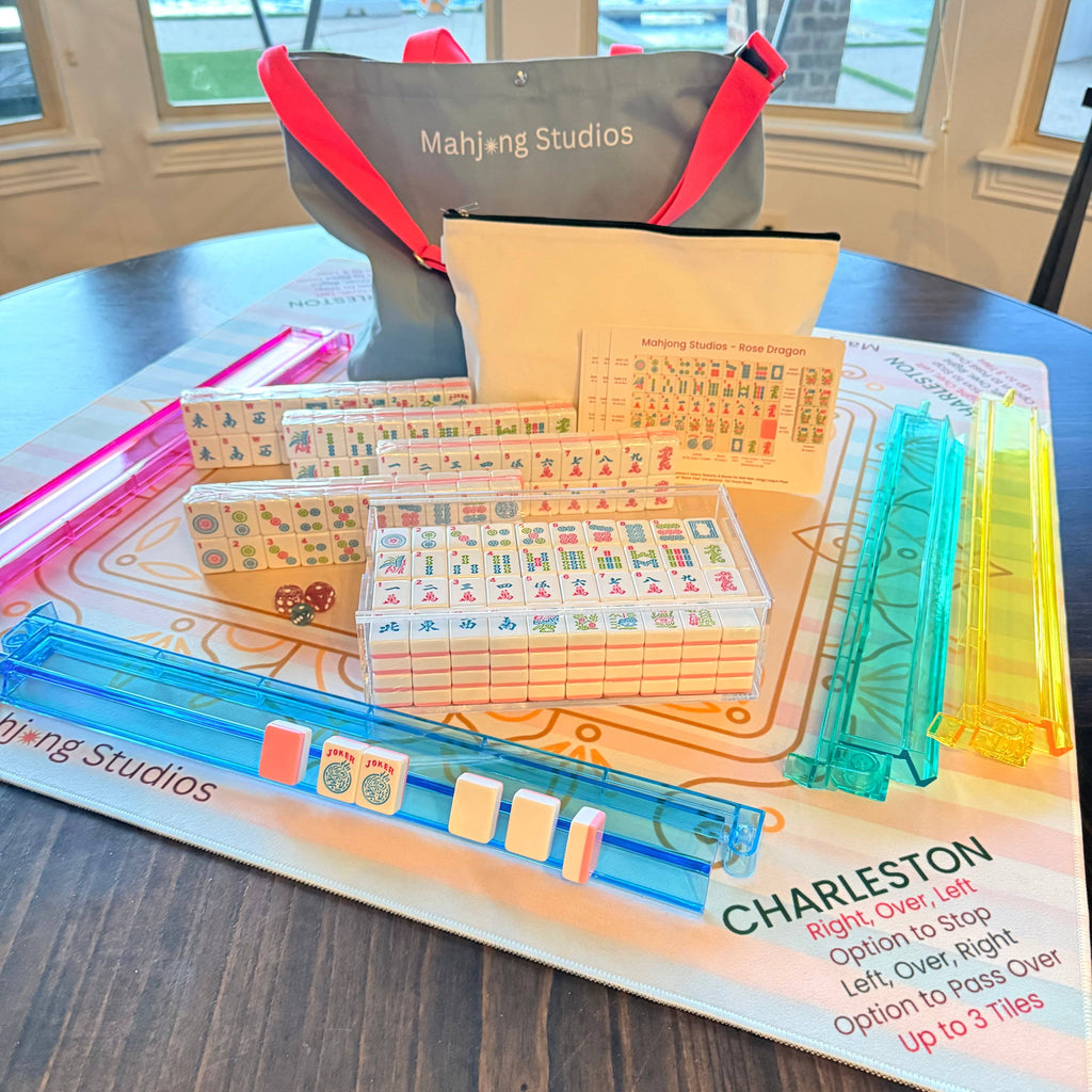 A Mahjong tile set arranged on a game mat, featuring colorful tiles, a carrying bag, and clear plastic tile racks.