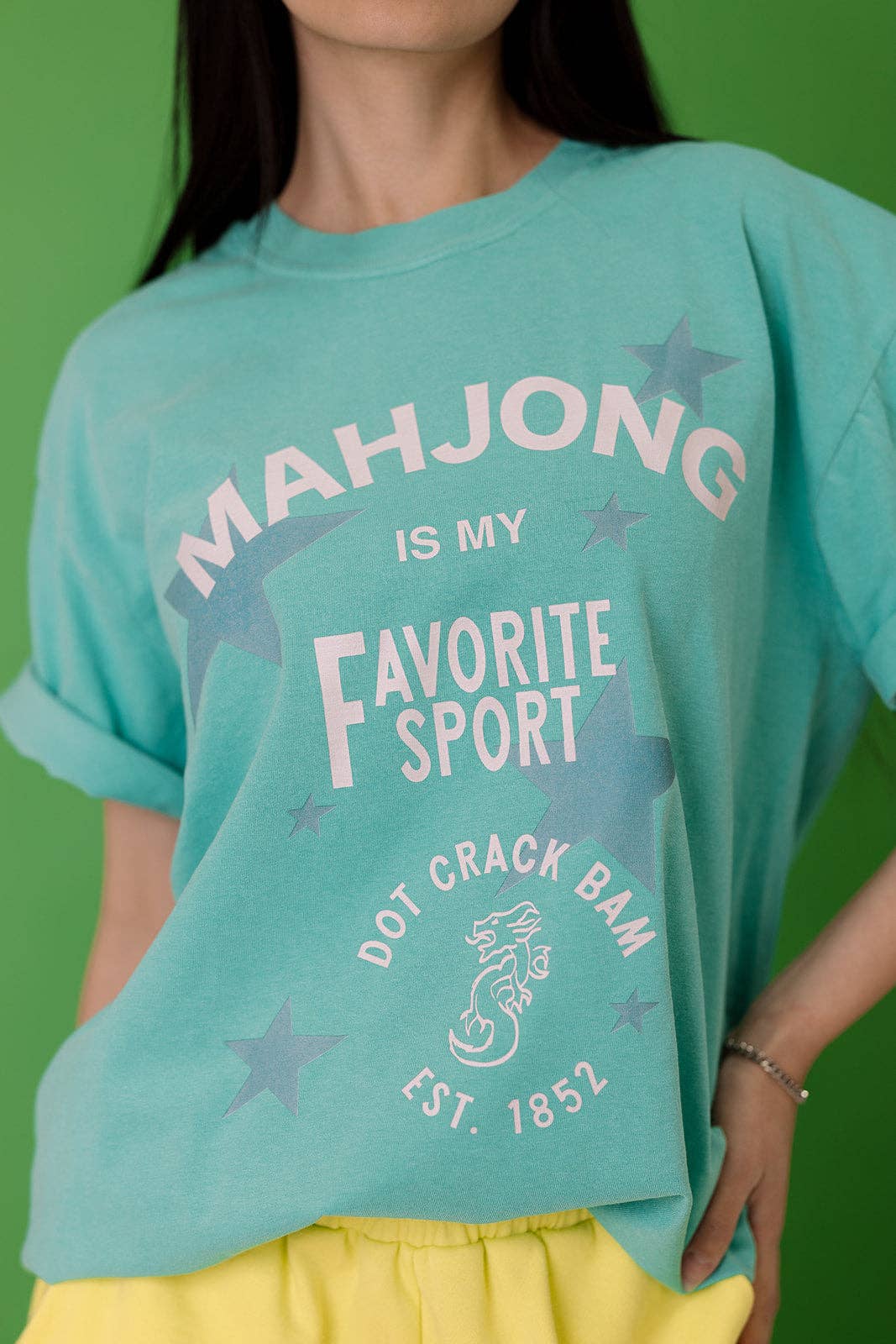 Turquoise tee with 'MAHJONG IS MY Favorite Sport' text and star graphics, featuring rolled sleeves and a relaxed fit.