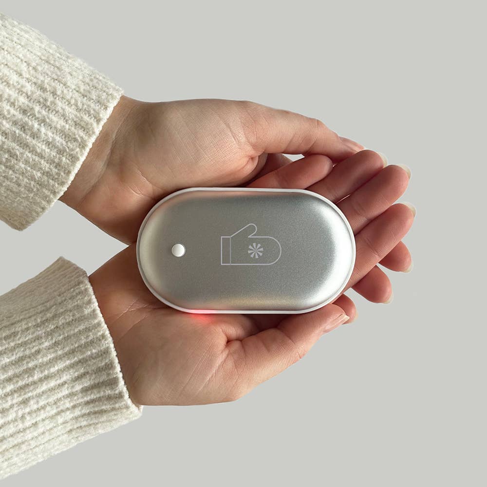 A person holding the Tech Candy eMitten hand warmer, showcasing its rounded rectangular shape and button with a light indicator.