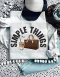 Light gray sweatshirt featuring the text 'SIMPLE THINGS' with illustrations of a drink and a handbag. Unisex fit for casual wear.
