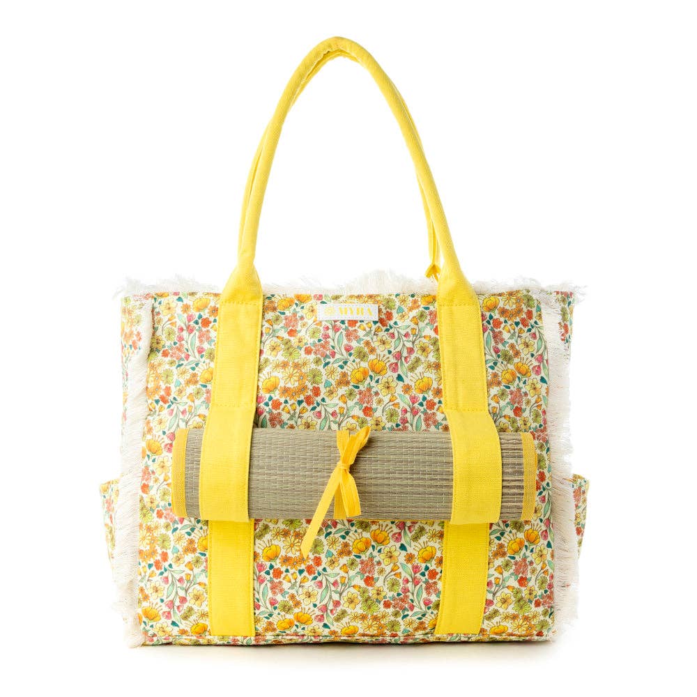 Wildflower print weekender bag with fringe detailing and desert blush carry straps, includes a rolled beach mat.