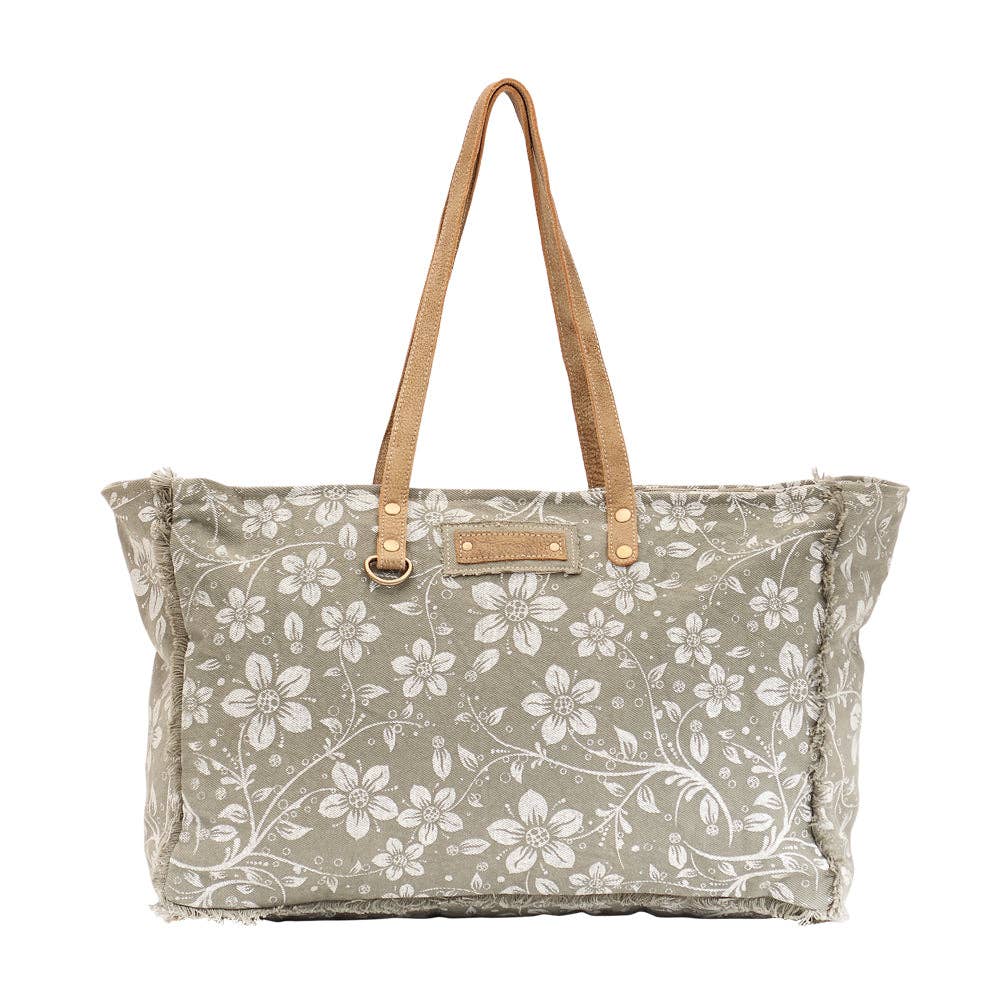 Floral weekender bag with light-colored flowers, tan handles, and a spacious design perfect for weekend getaways.