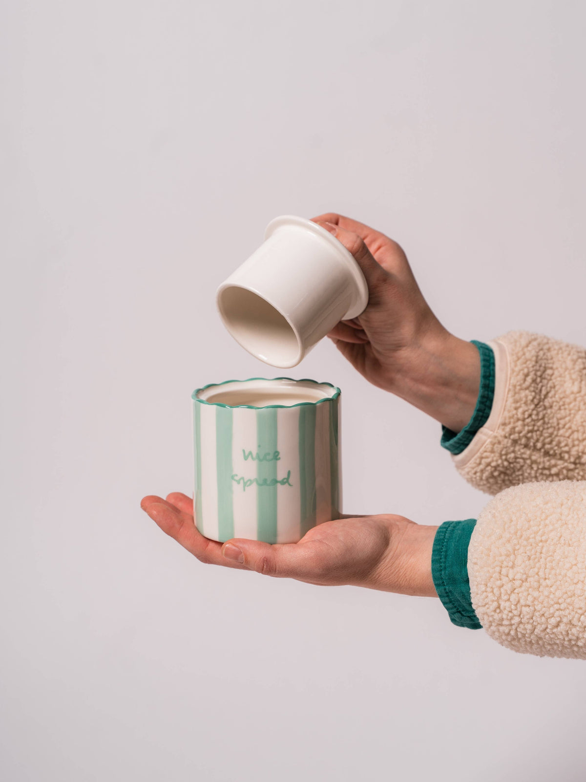 A person holds the Kinsey Scallop Butter Keeper featuring scalloped edges, vibrant stripes, and a cheerful saying.