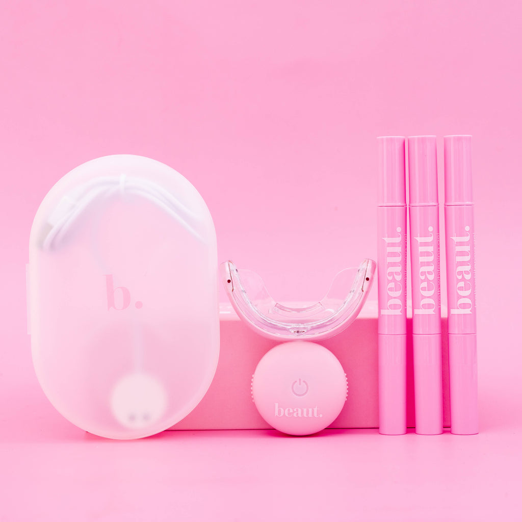 Polly Pink Kit featuring a pink device with a mouthpiece, control unit, and three smile pens for oral care and whitening.