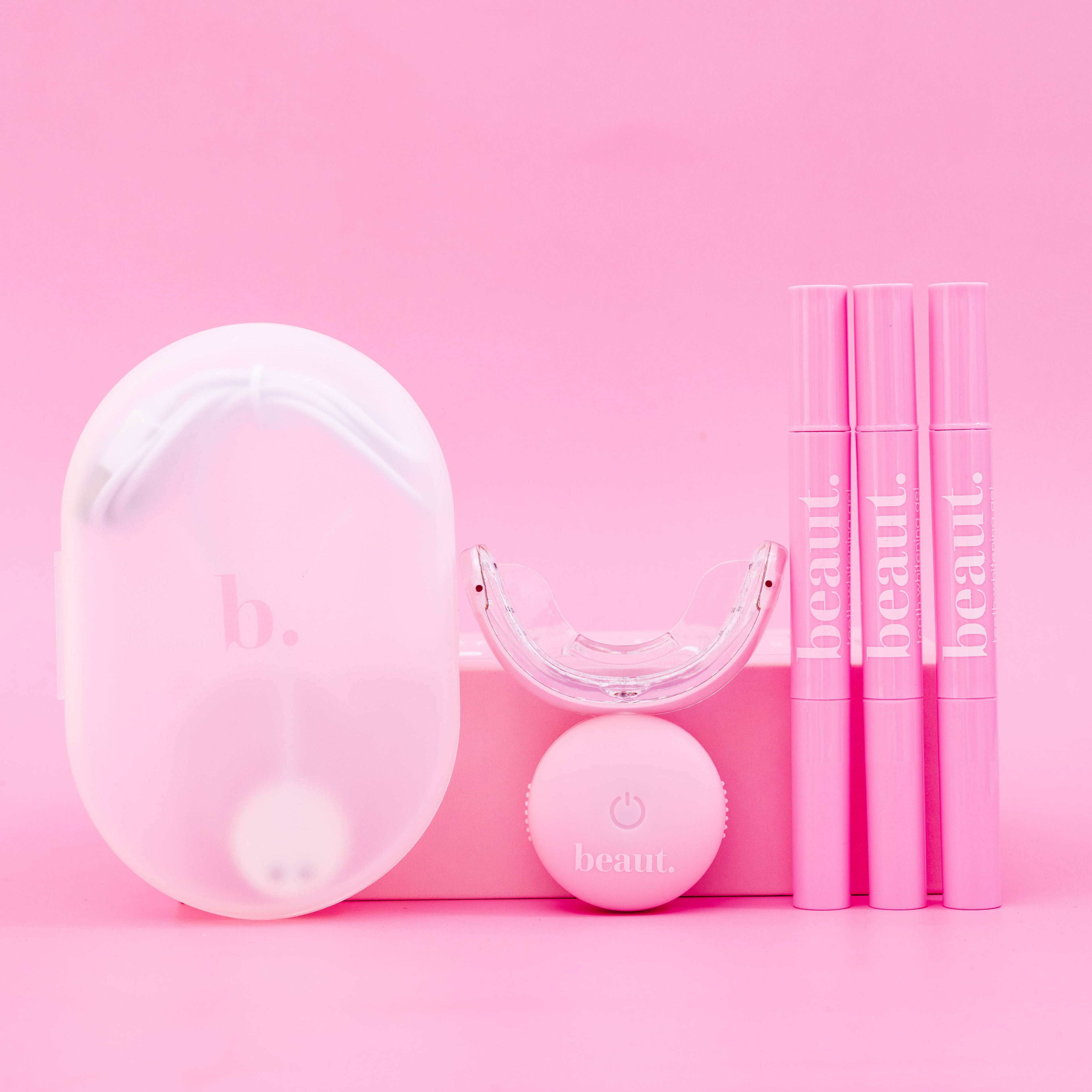 Polly Pink Kit featuring a pink device with a mouthpiece, control unit, and three smile pens for oral care and whitening.