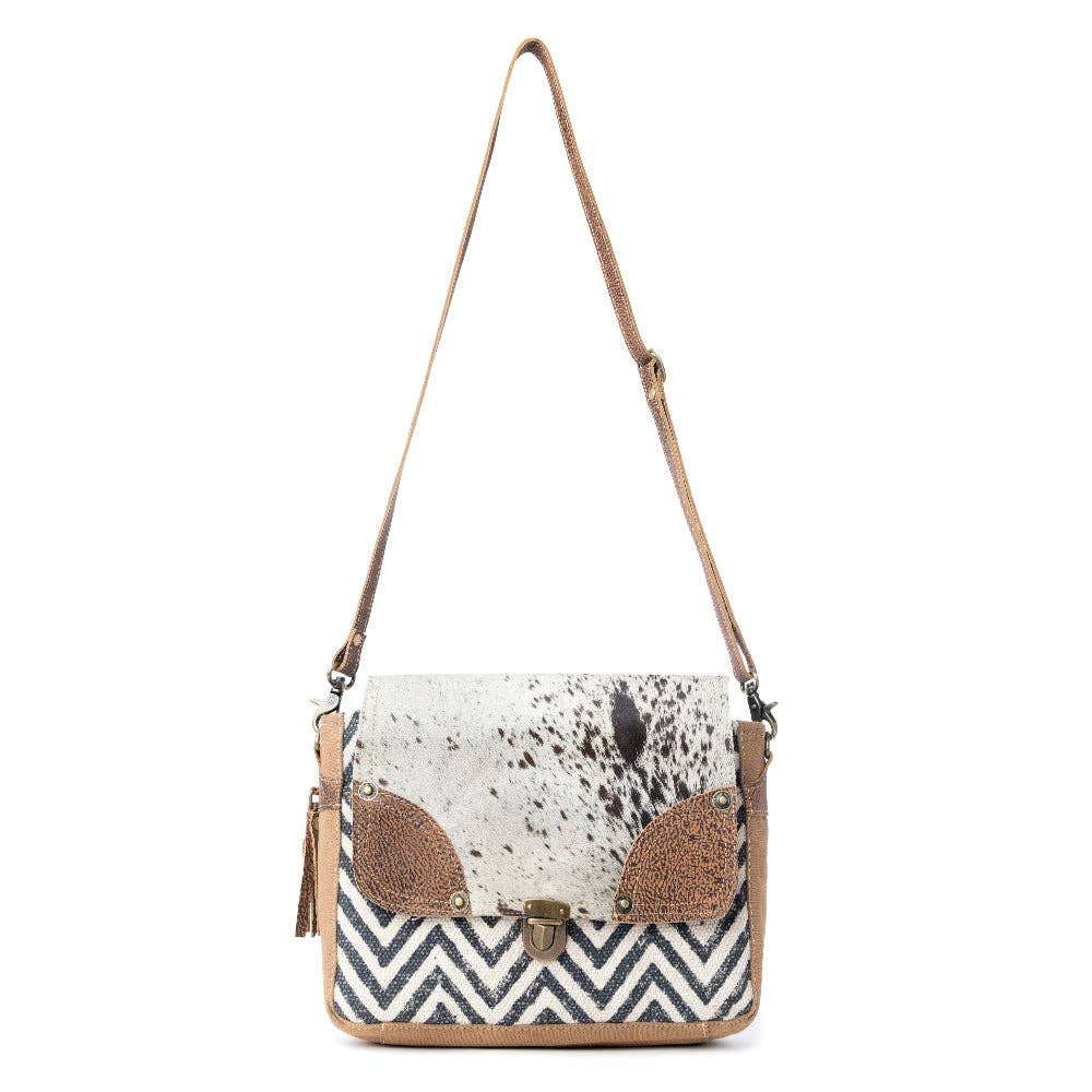 Rugged messenger bag featuring a hairon flap, chevron design, and neutral tones with a shoulder strap and clasp closure.