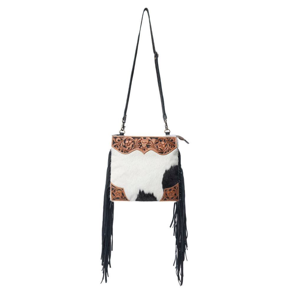 Hand-tooled caramel leather bag with hair-on hide front, black leather side fringe, and adjustable shoulder strap.