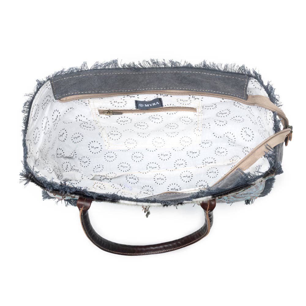 Articulate Canvas & Hairon Bag featuring a frayed edge, leather handle, and patterned lining with a zippered pocket.