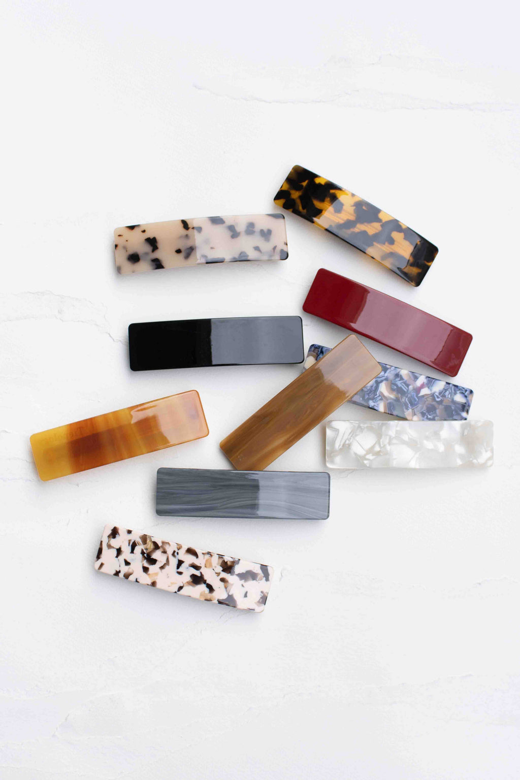 A collection of sleek rectangular hair barrettes in various colors and patterns, including marbled designs and solid hues.