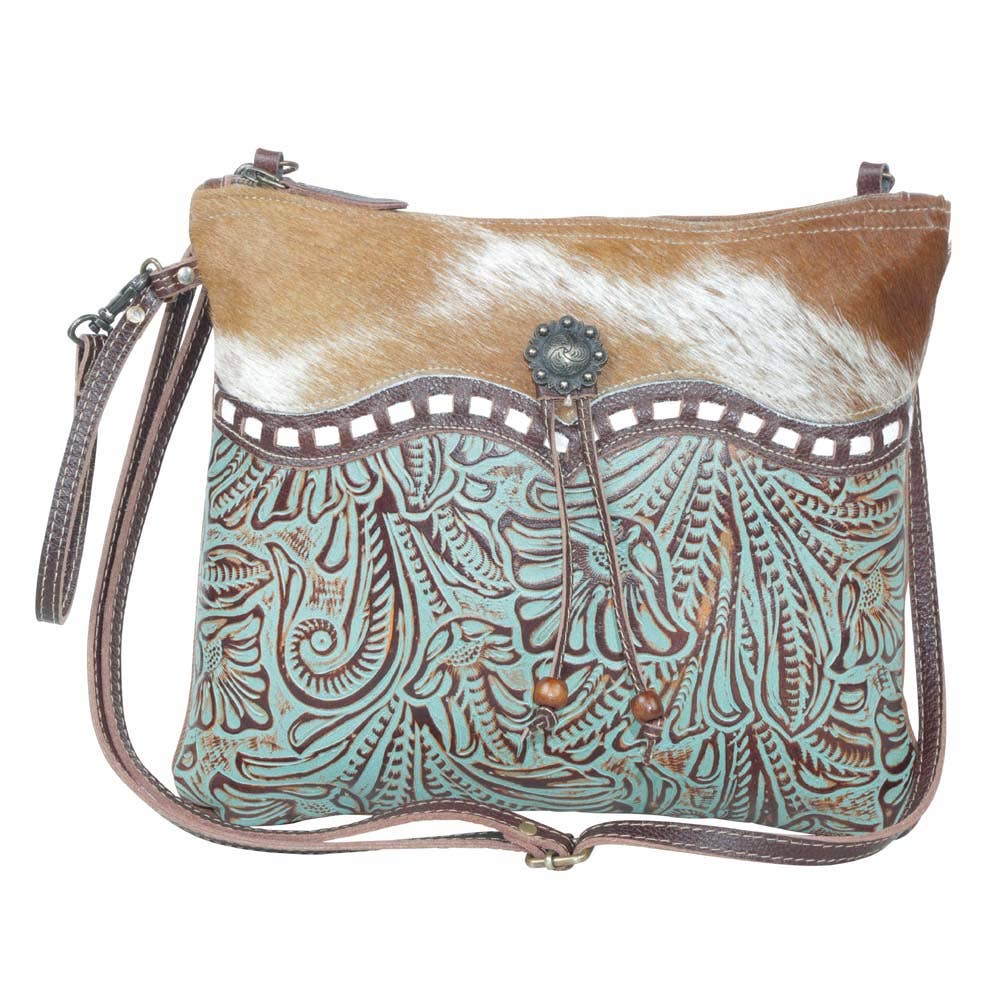 Turquoise embossed leather crossbody bag with brown-and-white cowhide back and decorative beads on the closure.