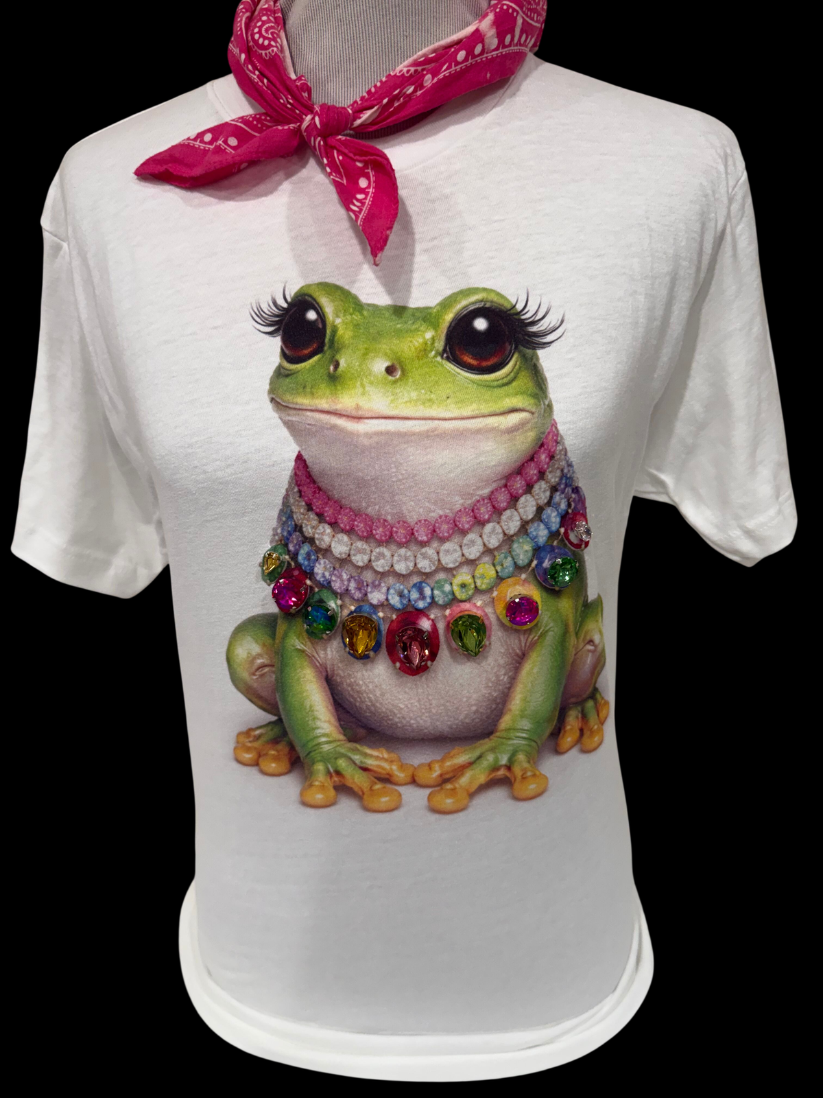 A white t-shirt featuring a frog with a jeweled collar and colorful embellishments around its neck.