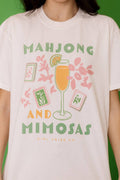 Light-colored tee featuring the graphic "MAHJONG AND MIMOSAS" with a cocktail glass and decorative elements.
