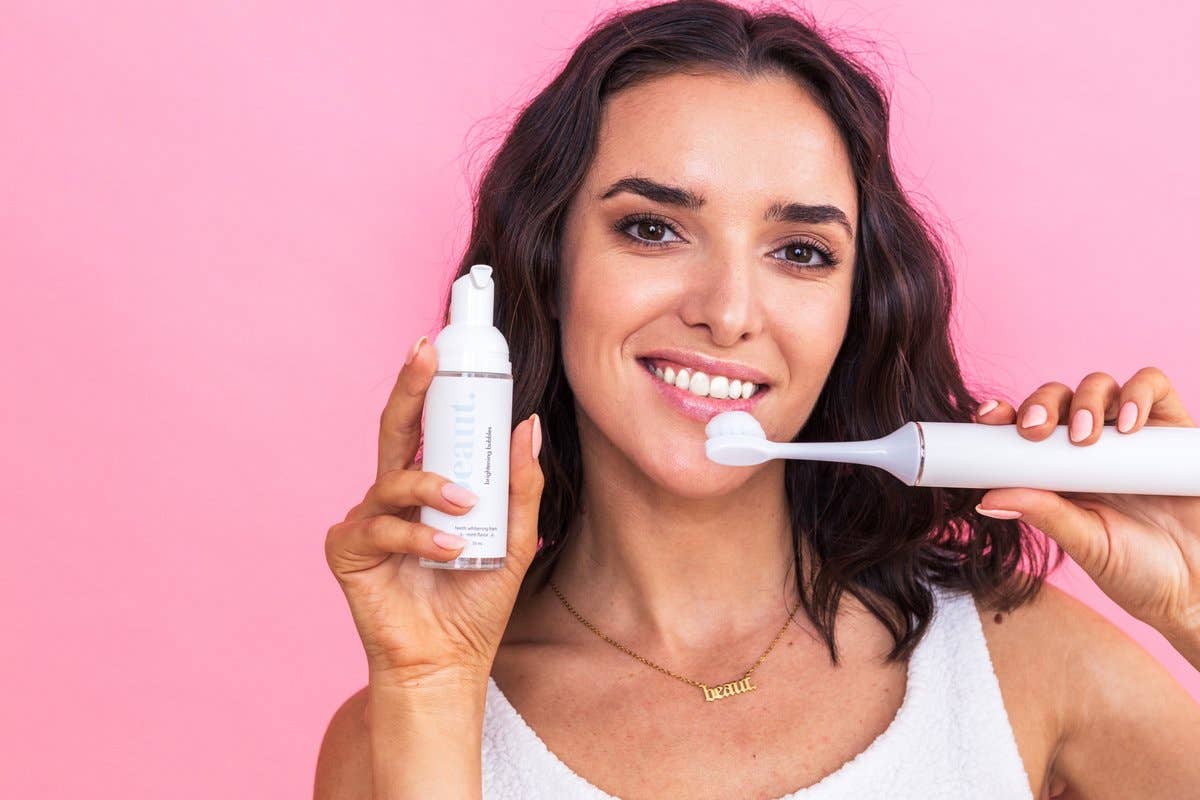 A person holding a bottle of Brightening Bubbles and a toothbrush with foam, ready for a bright smile.
