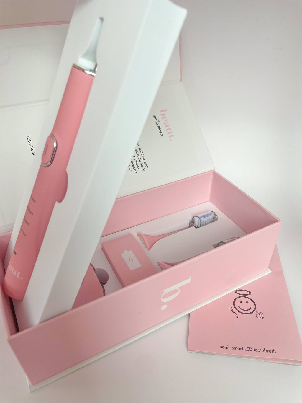 A pink Smile Kleen Sonic Vibration Toothbrush with its accessories displayed in light pink packaging.