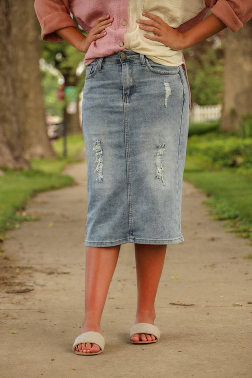 Knee-length denim skirt with front distressing, featuring a zipper and button closure, front and back pockets.