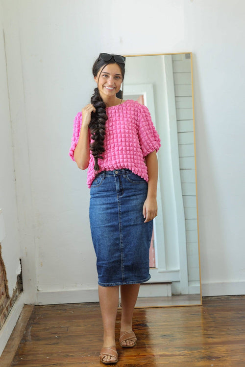 A woman showcases a knee-length dark denim skirt with a fitted silhouette, featuring a zipper and button closure.