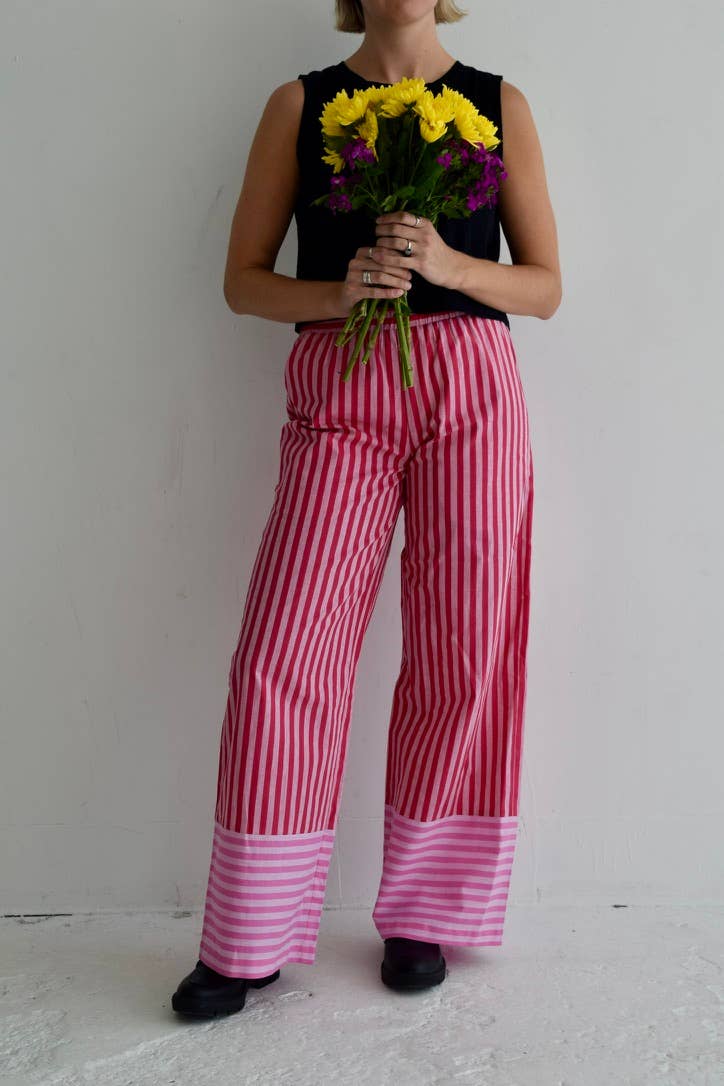 Vertical pink and red striped pants with a solid pink hem, featuring a loose fit and elastic waistband.