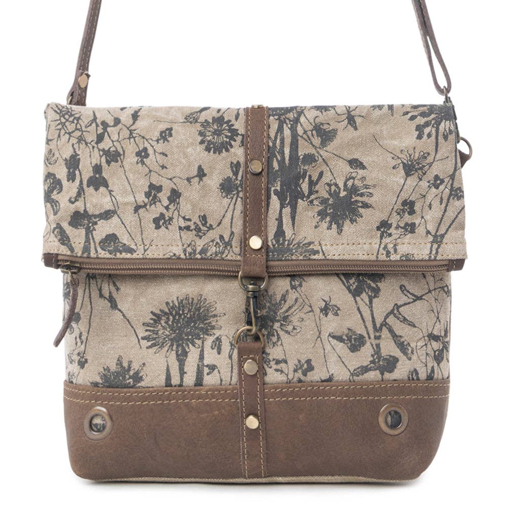 Floral crossbody bag featuring a light canvas with a chocolate leather bottom, fold-over flap, and adjustable strap.