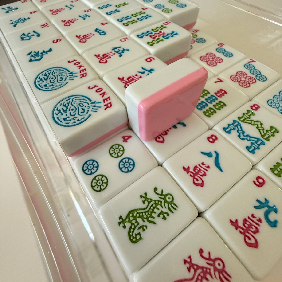 Colorful Mahjong tiles arranged in a grid, featuring a prominent pink 'JOKER' tile with glossy finishes and intricate designs.