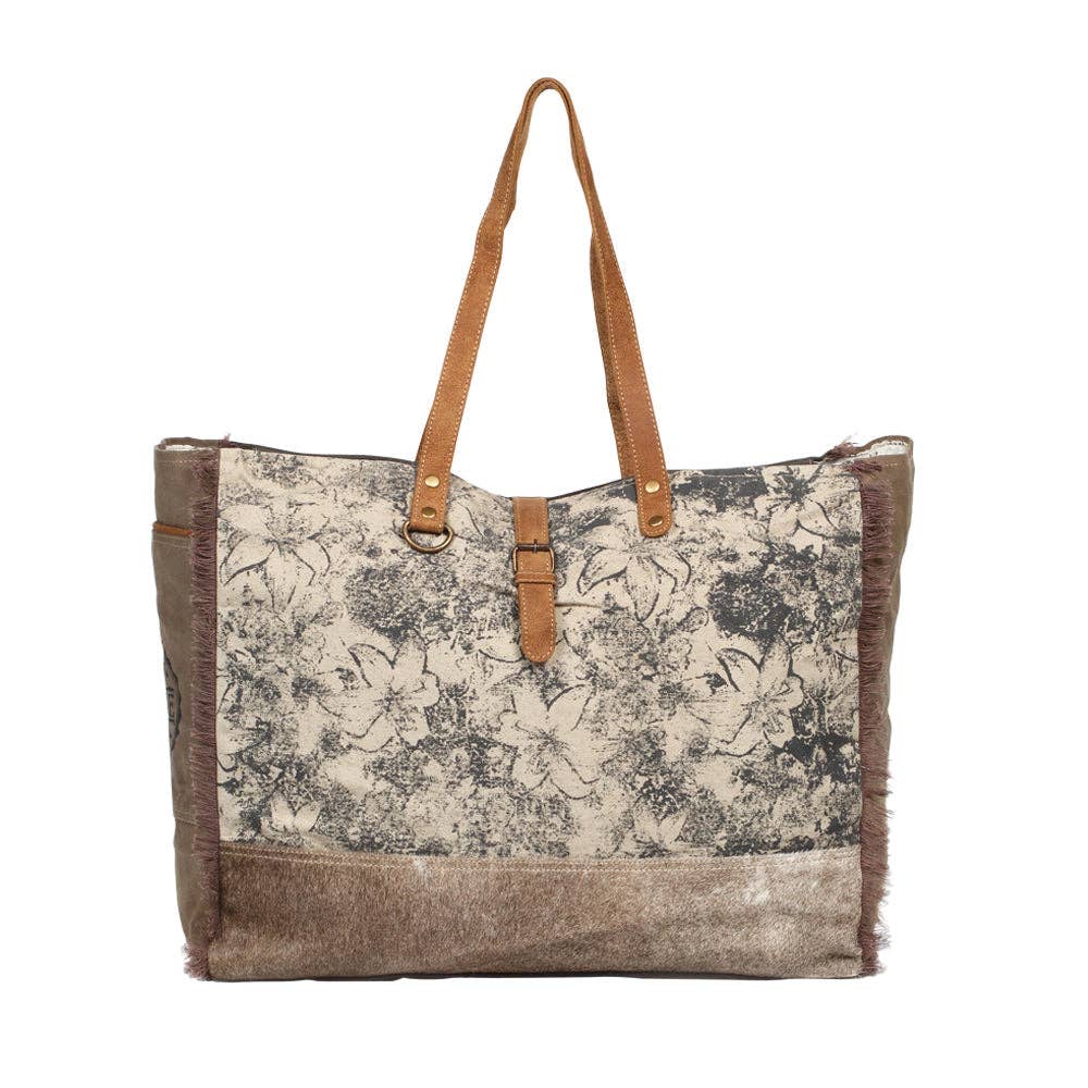 Floral canvas weekender bag with leather and hairon accents, featuring two top handles and a zipper closure.