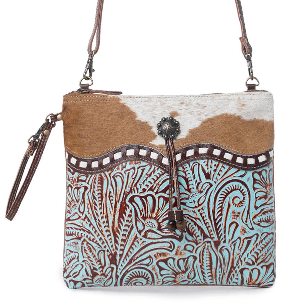 Turquoise embossed leather crossbody bag with a brown-and-white cowhide accent and a stylish wrap-around design.