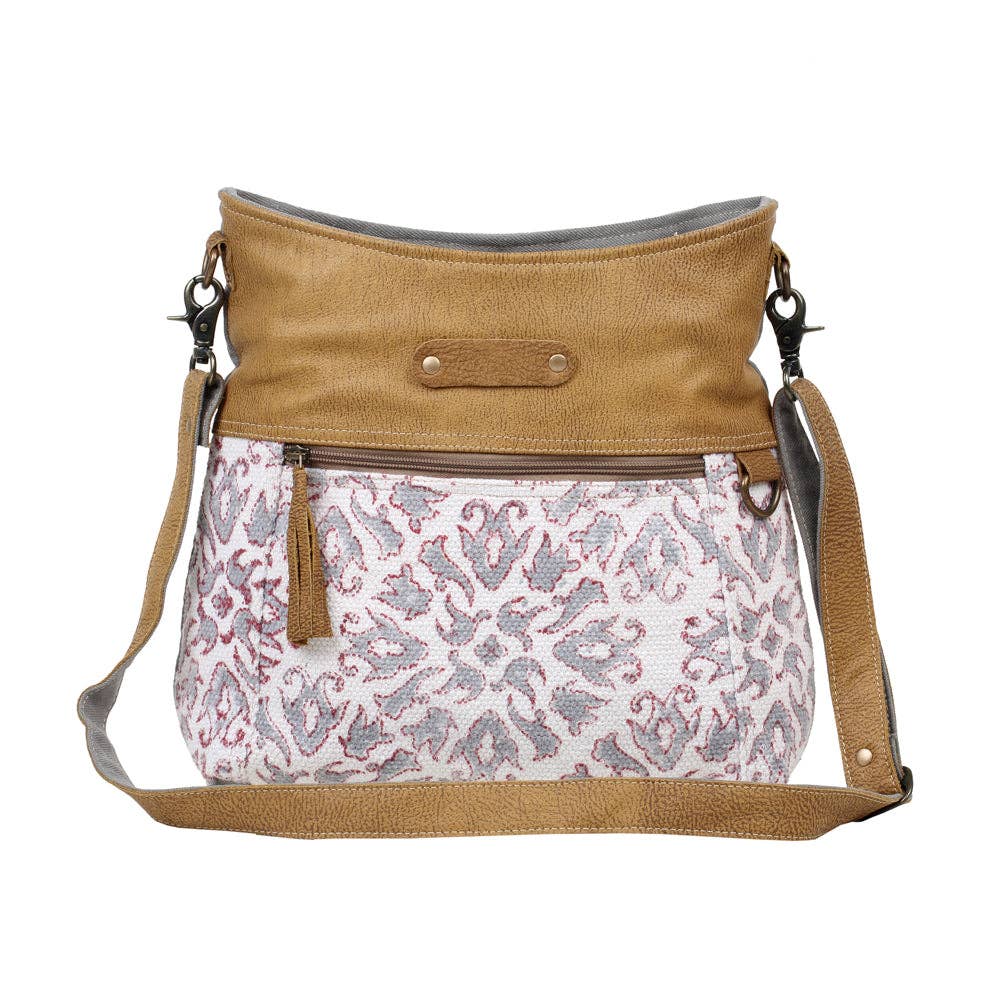 Shoulder bag featuring a patterned front and solid top, with an adjustable leather strap and zippered pocket for functionality.