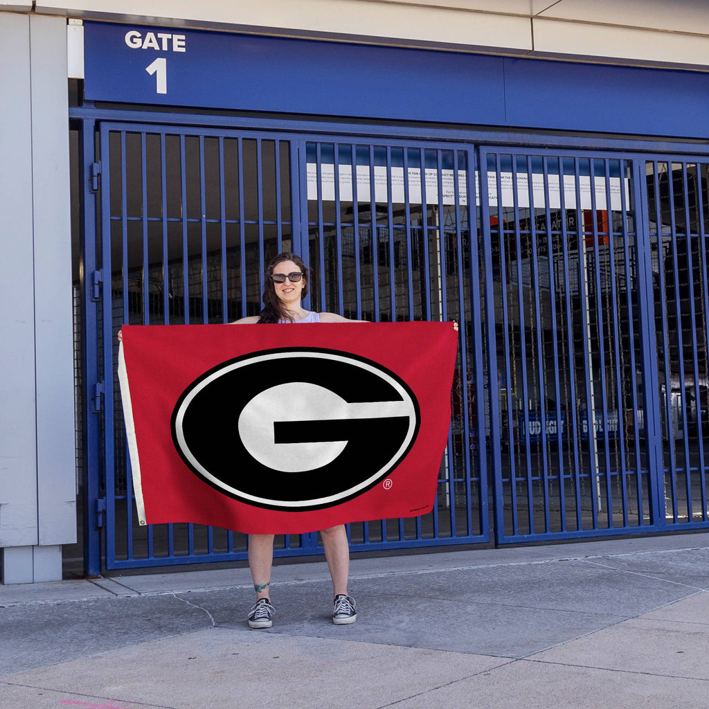 A person holding a Georgia Oval G banner flag with bright graphics, perfect for showing team pride on game day.