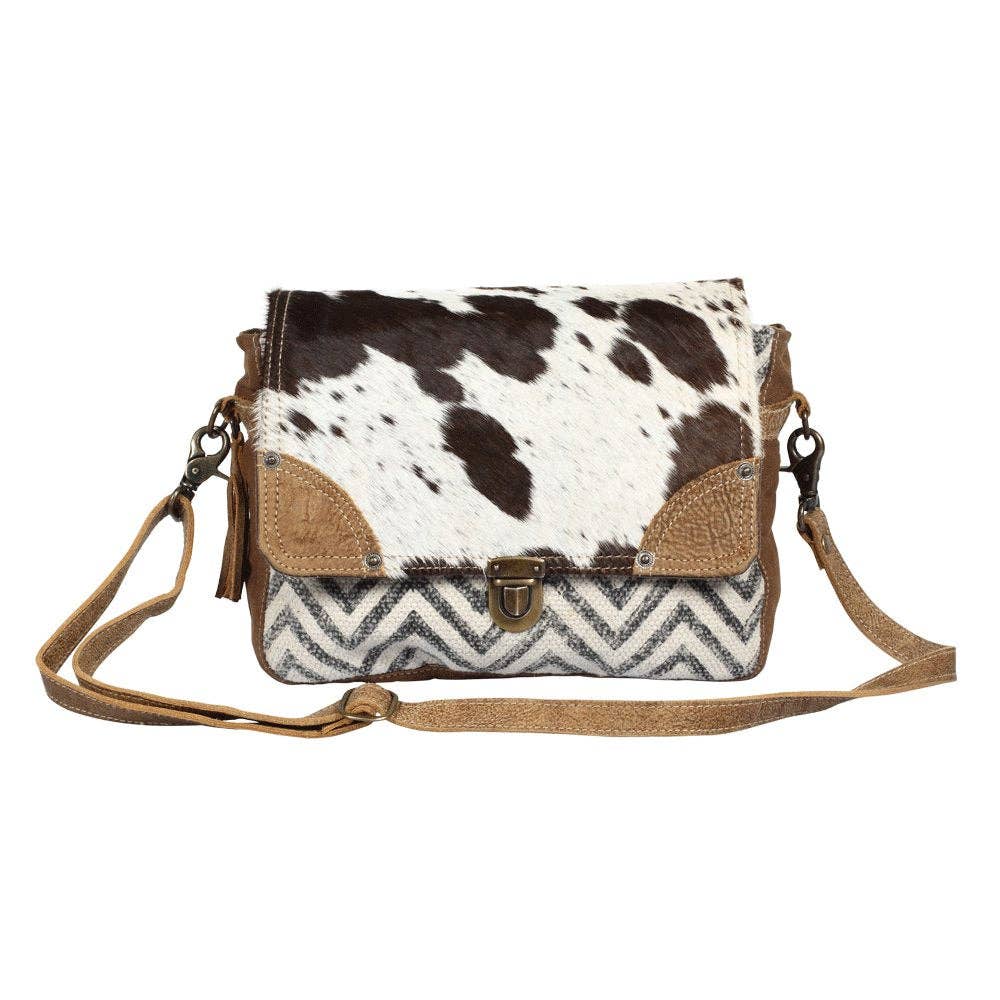 Rugged messenger bag featuring a hairon flap with a spotted pattern, chevron design, and leather accents in browns and creams.
