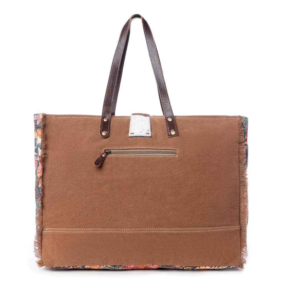 Floral design weekender bag with a brown base, two handles, and fringe detail along the edges. Perfect for weekend adventures.