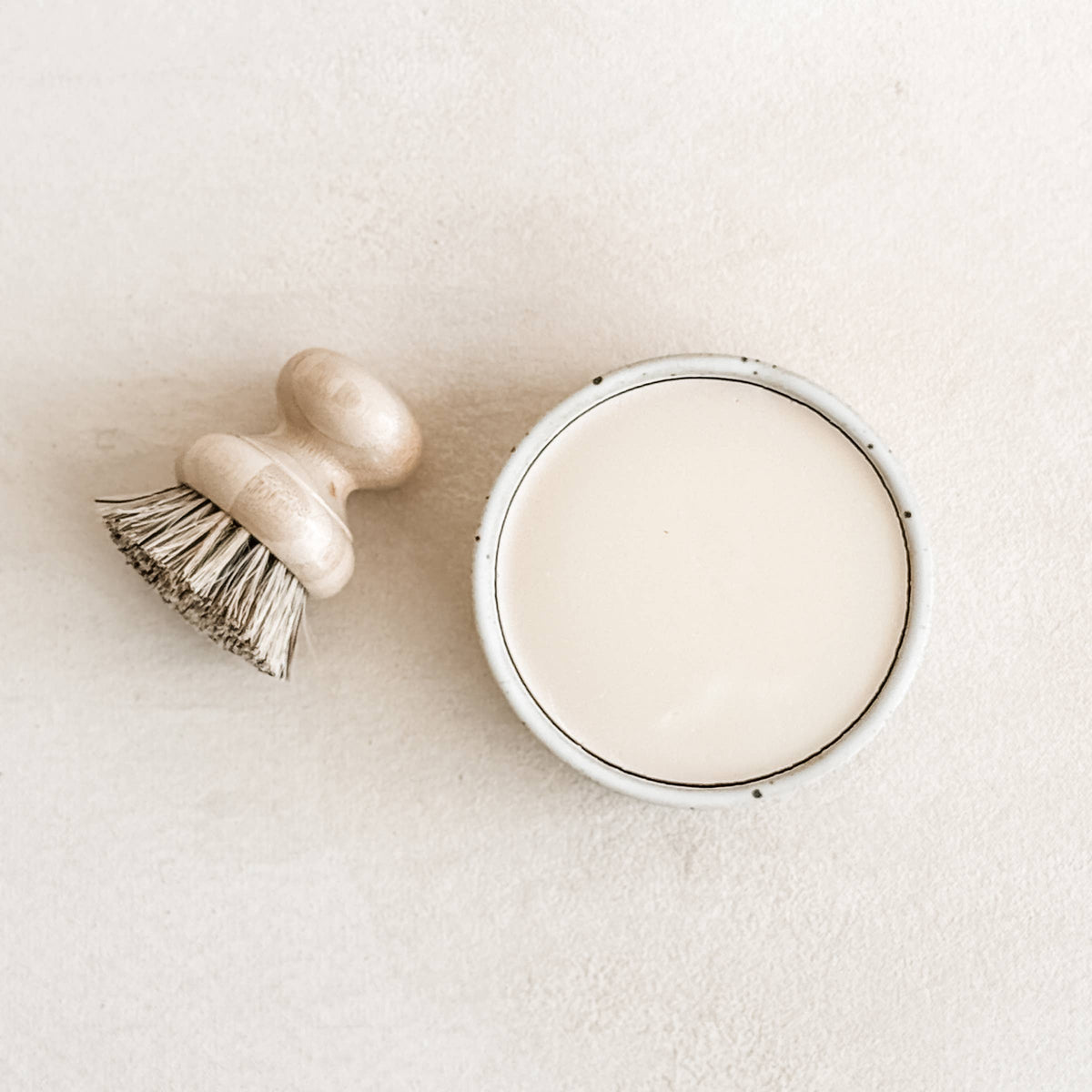 Round, light-colored dish soap container with a wooden brush, featuring a simple design for natural cleaning.