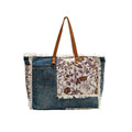 Floral cotton weekender bag featuring fringe detailing and a brown leather shoulder strap, perfect for your next adventure.