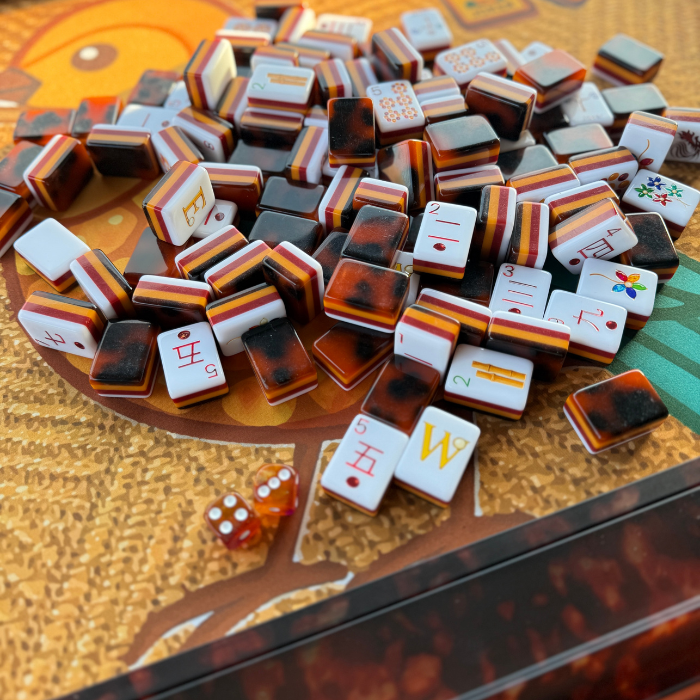 A collection of colorful mahjong tiles with a tortoise shell pattern, showcasing various symbols and two visible dice.
