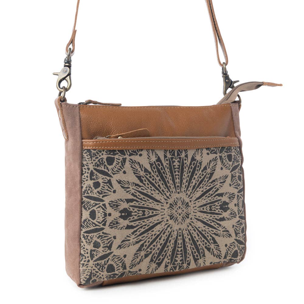 Small crossbody bag featuring a decorative front pocket and leather top section, perfect for carrying essentials.