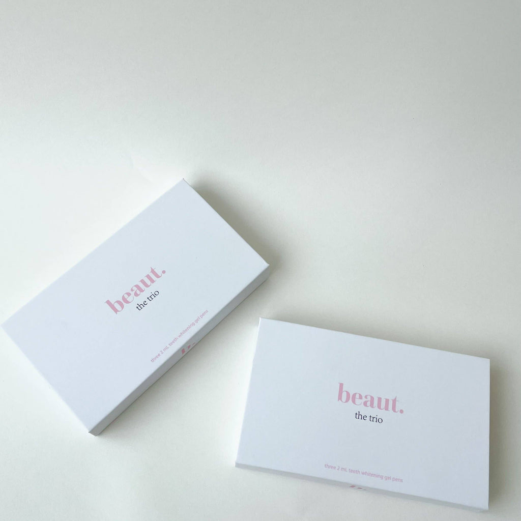 Minimalistic white box labeled 'the trio' with a pink logo, featuring two visible smile pens for teeth whitening.