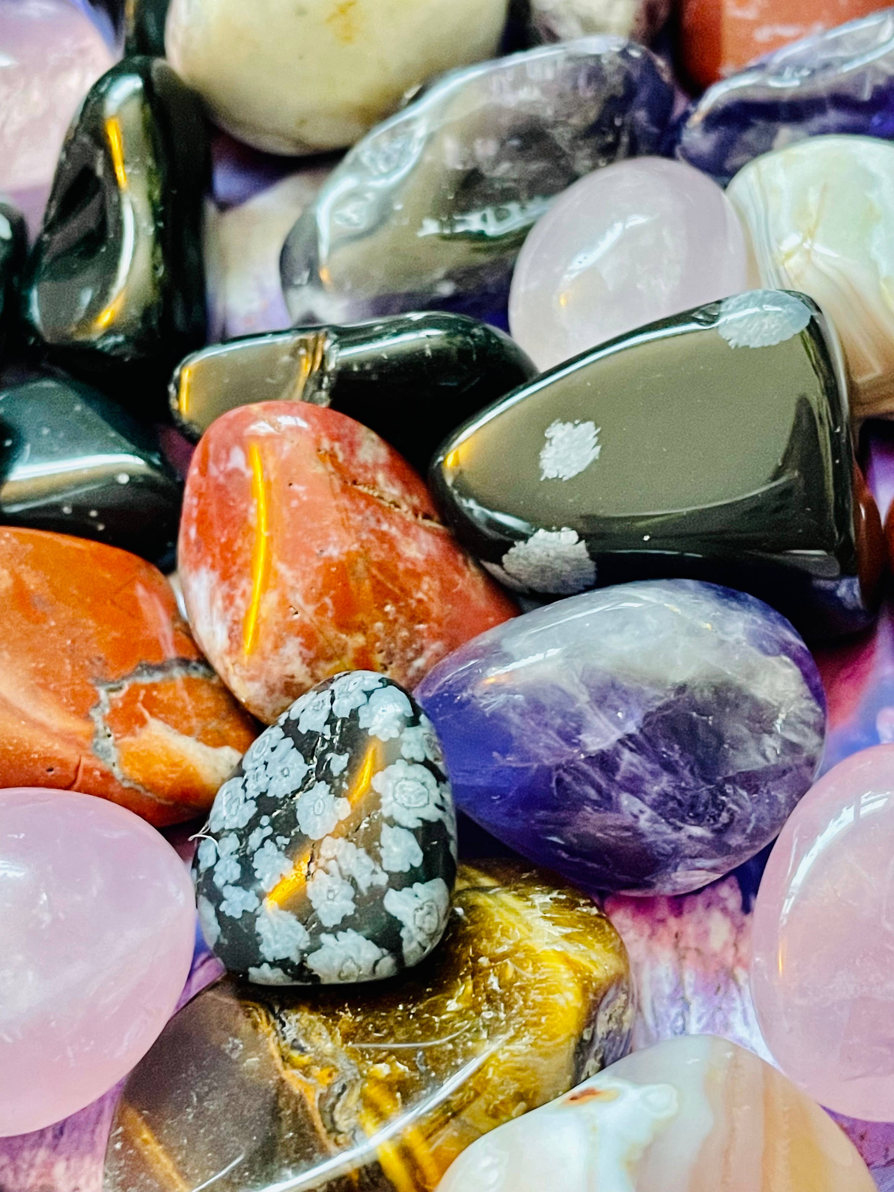 A collection of polished crystal tumble stones in various colors, showcasing their unique shapes and radiant hues.