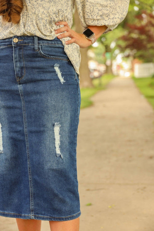 Knee-length denim skirt with a fitted silhouette, featuring distressed patches and a zipper and button closure.