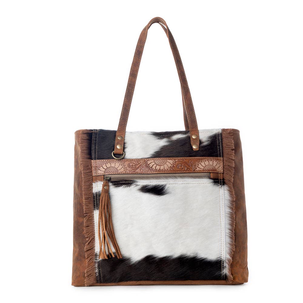 Large neutral handbag featuring canvas and hairon materials, with fringe detailing and an adjustable leather strap.