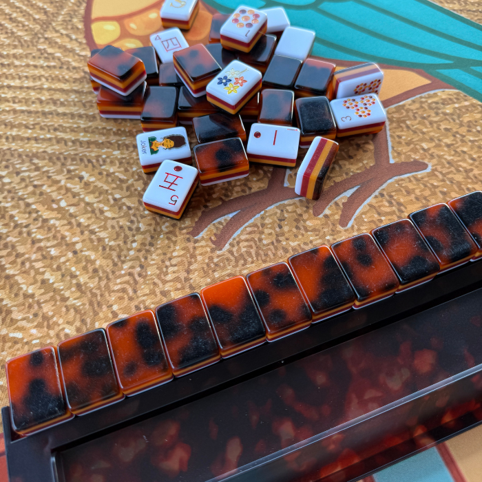 Tortoise shell Mahjong rack with a glossy finish and scattered colorful Mahjong tiles. Perfect for game nights.