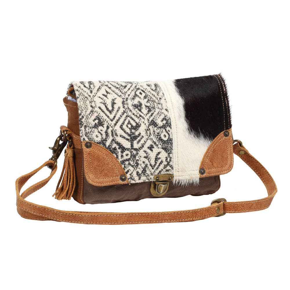 Geometric flap messenger bag featuring black-and-white hairon cowhide, tan leather corners, and a playful layered tassel.
