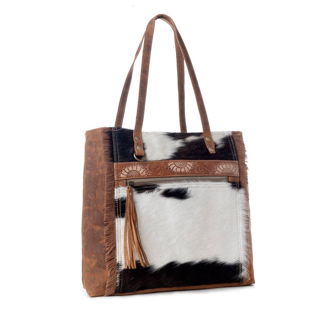 Large neutral handbag featuring canvas and hairon materials with fringe details and an adjustable leather strap.