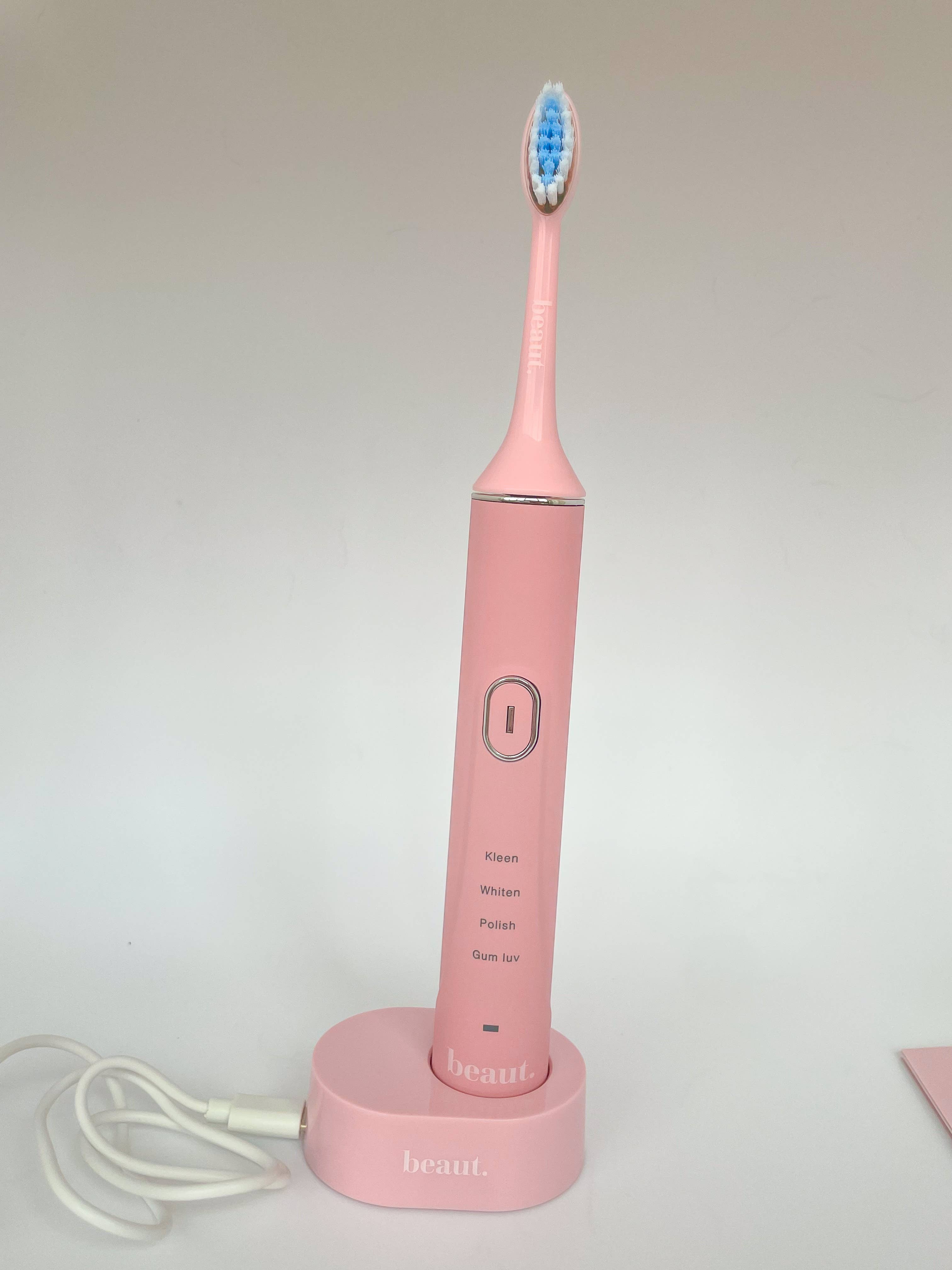 Pink Smile Kleen Sonic Vibration Toothbrush with blue and white bristle head and charging base.