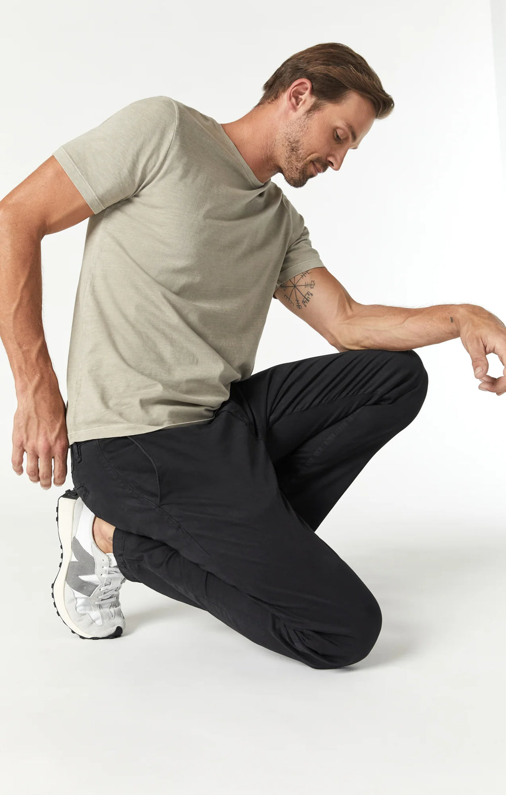 A man wearing slim-fit black chino pants styled casually with a light-colored t-shirt and athletic shoes.