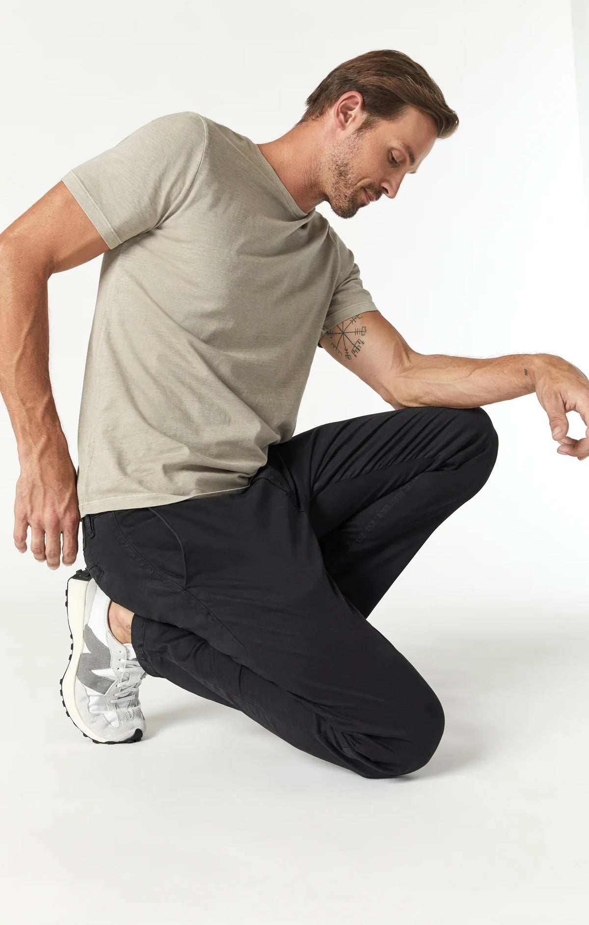 A man wearing slim-fit black chino pants styled casually with a light-colored t-shirt and athletic shoes.