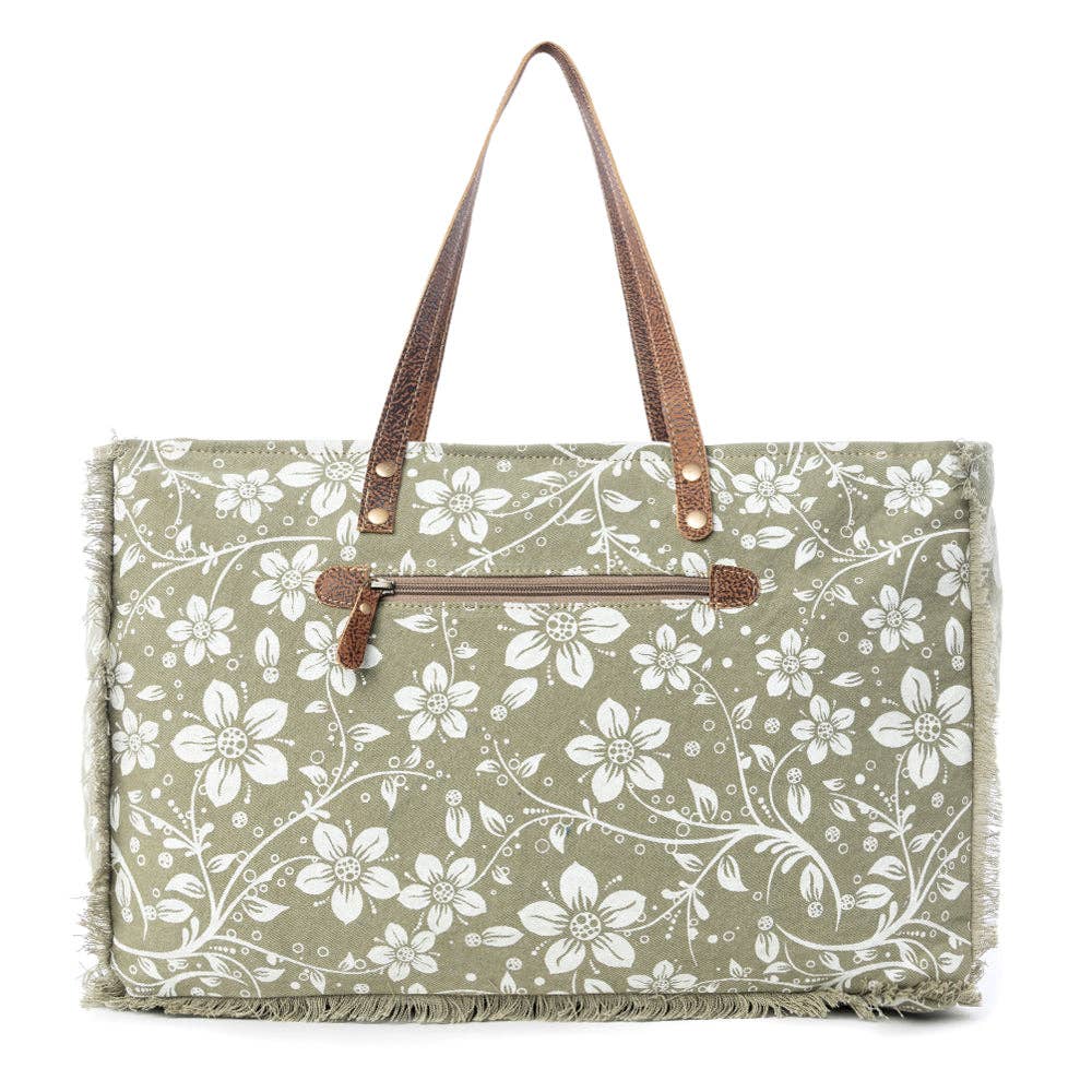 Floral weekender bag with a light green background, leather top handles, and zipper closure, featuring frayed edges.