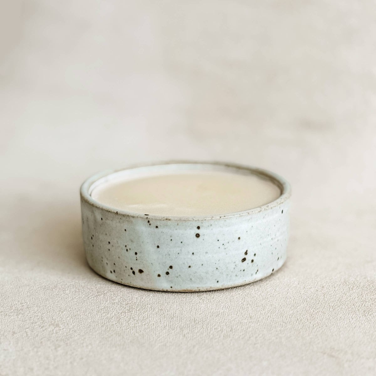 Round, speckled light gray stoneware container filled with creamy solid dish soap, perfect for natural cleaning.