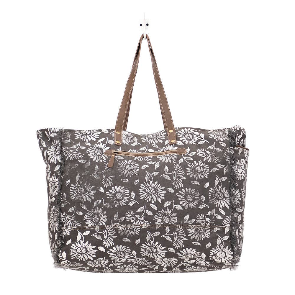 Floral weekender bag with leather top handles and zipper closure, featuring spacious compartments and exterior pockets.