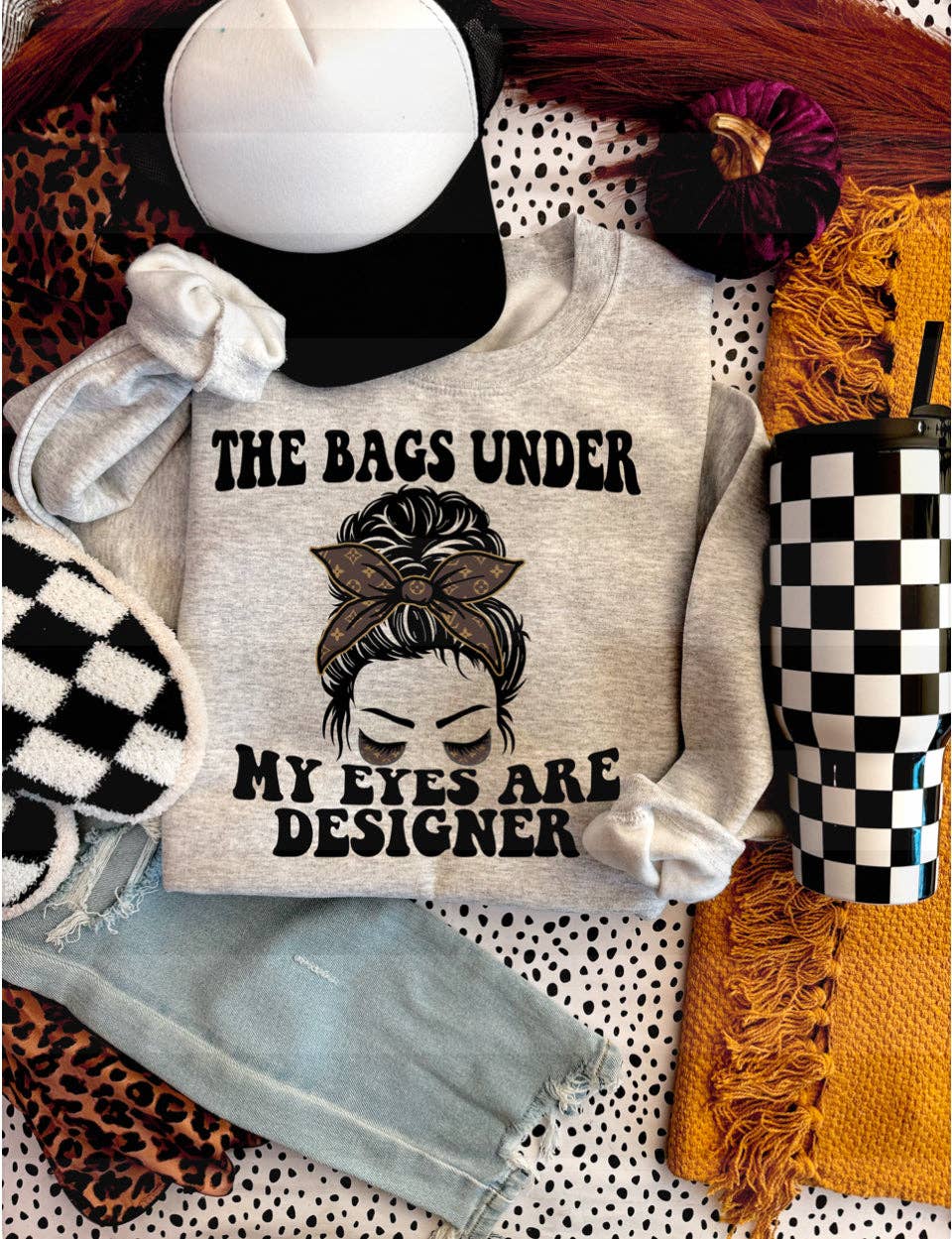 Light gray sweatshirt featuring the text 'THE BAGS UNDER MY EYES ARE DESIGNER' with a stylish graphic design.