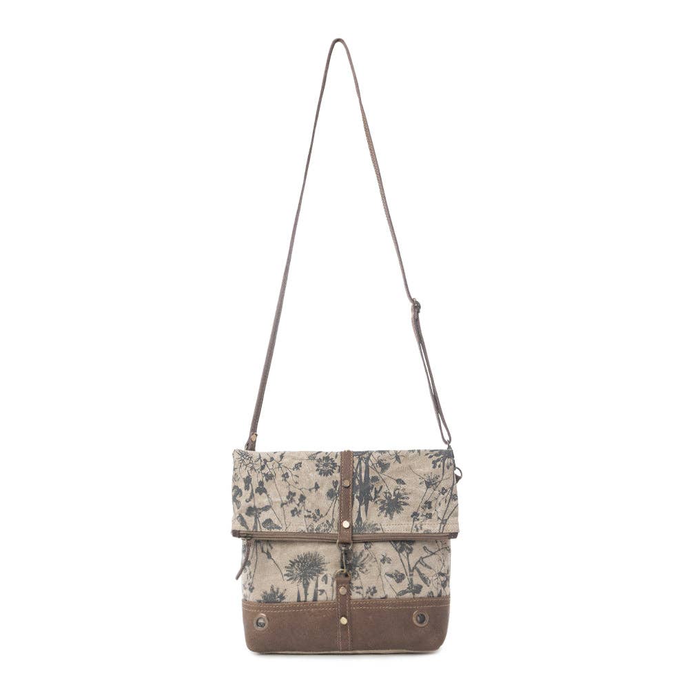 Floral crossbody bag featuring a chocolate leather bottom panel, fold-over flap with zipper closure, and adjustable shoulder strap.