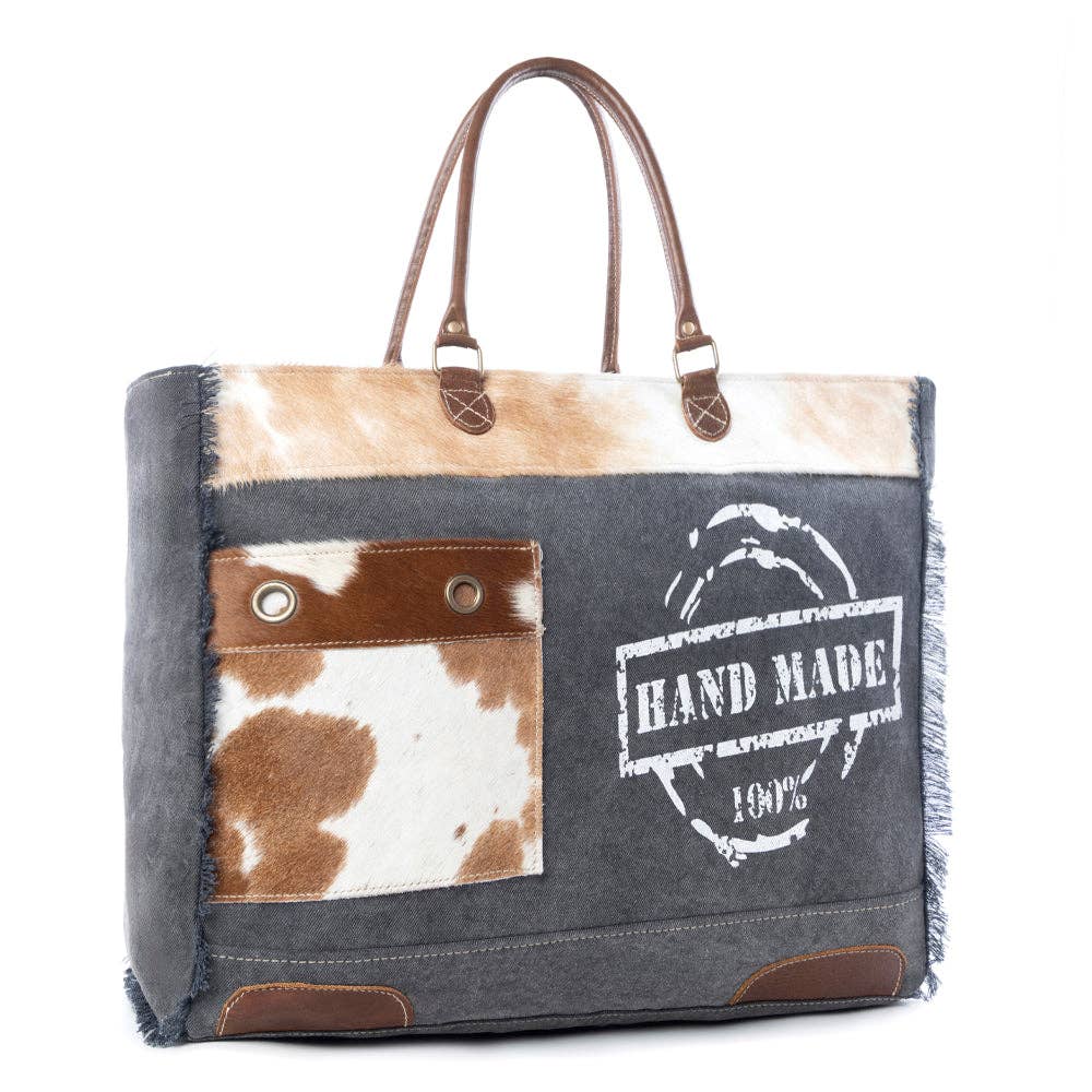 Handmade Print Weekender Bag featuring a cowhide pattern, leather top handles, and a front pocket with snap closures.