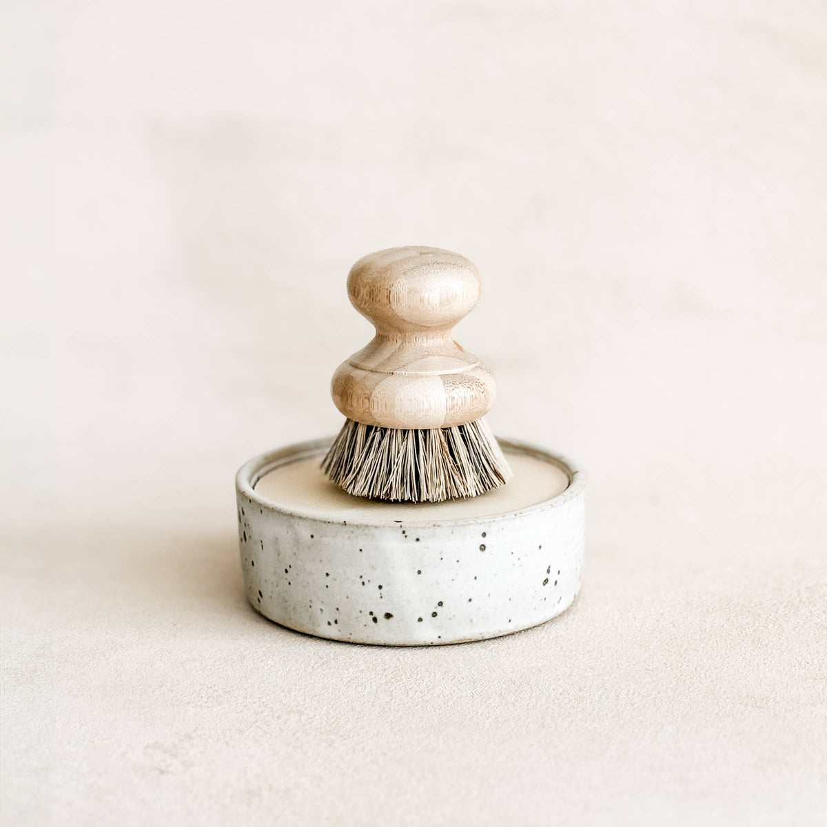 Round speckled stoneware container with solid dish soap and a wooden brush on top, designed for effective dish cleaning.